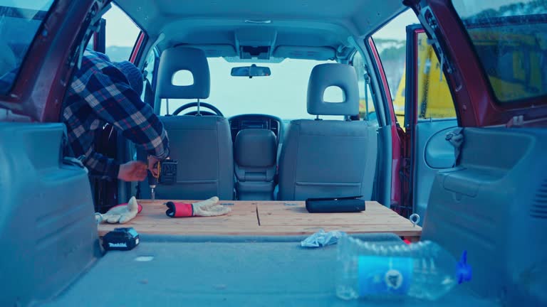 A Person is Working Inside a Red Van, Using a Power Drill to Secure a Wooden Platform in the Back - Close Up