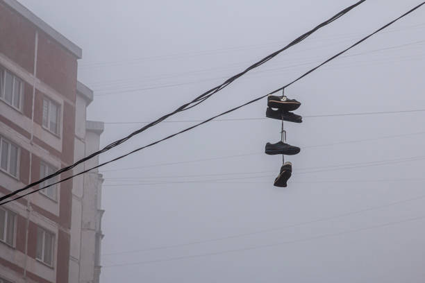 sports shoes hanging on an electric wire. The wire runs horizontally against a clear blue sky. The shoes are tied together with laces and hang in the middle of two lines.