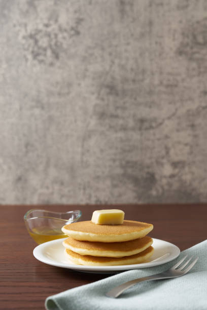 Two pancakes with butter on a plate on a wooden table.