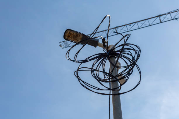 Streetlight pole with tangled wires against blue sky and construction crane in background
