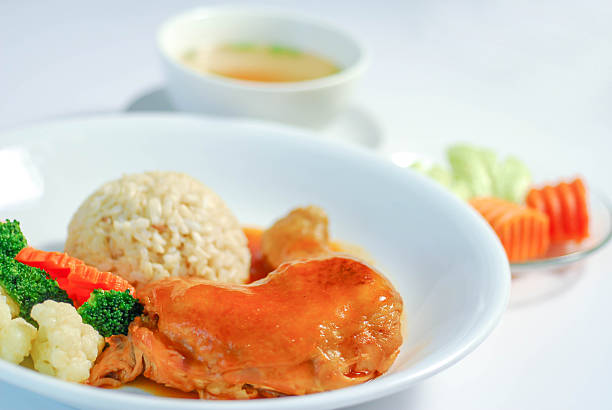 Red Braised Chicken with Rice and Steamed Vegetables, Red braised chicken served with steamed rice, mixed vegetables, and clear soup on a white plate. Clean background