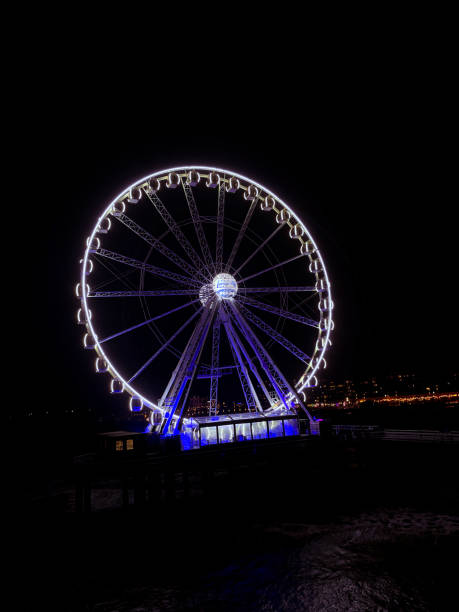 A Ferris wheel illuminated with bright lights stands against the dark night sky. The vibrant colors and geometric structure create a striking visual contrast