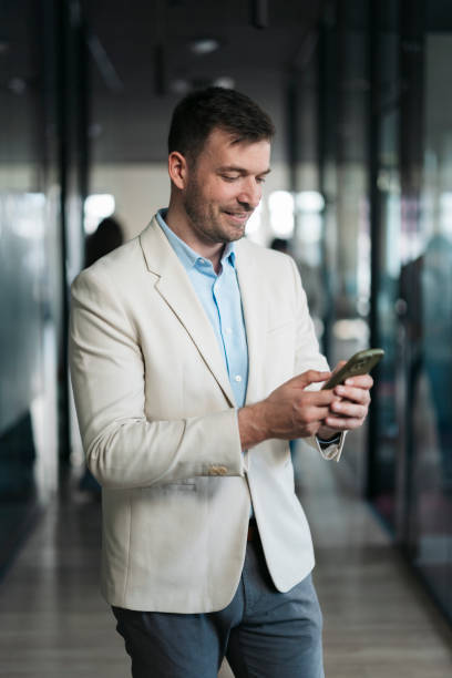 istock Businessman smiling and using smartphone in office corridor 2206478263