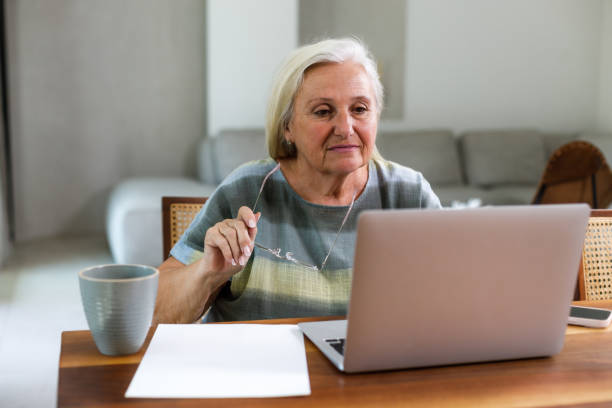 istock Confident senior woman using laptop and smiling while working late at home 2206478347