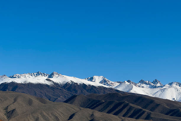 Clear skies crown a dramatic contrast of green hills and icy peaks.