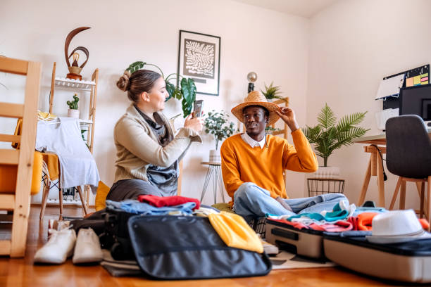 istock Young adults packing at home in suitcase preparing for trip and enjoying it while trying on hats they want to bring 2206481372