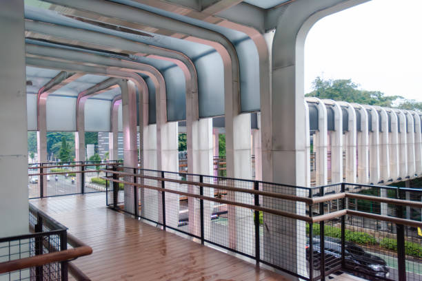 Stock image of a modern public pedestrian crossing bridge featuring a sturdy square truss frame design. Captured from a ground-level perspective, this image highlights the geometric structure and urban architectural appeal. Ideal for topics related to city infrastructure, urban design, pedestrian safety, and transportation development. Perfect for editorial, commercial, and web use.