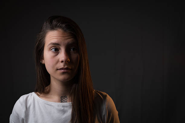 A captivating studio portrait of a young Caucasian woman illuminated by striking dual lighting. A crisp white side light sculpts her facial features, highlighting her expression of surprise and intrigue, while a soft warm backlight gently outlines her profile against the deep black background. Her gaze directed slightly off-camera creates a sense of mystery and curiosity. This expertly lit portrait with its play of cool and warm tones is perfect for storytelling concepts, editorial features, or advertising requiring emotional depth and cinematic quality.