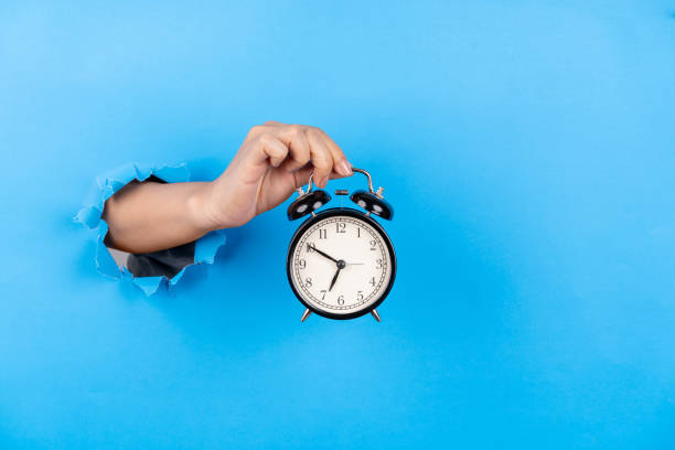 istock Female hand holding alarm clock through a blue paper background 2206486741