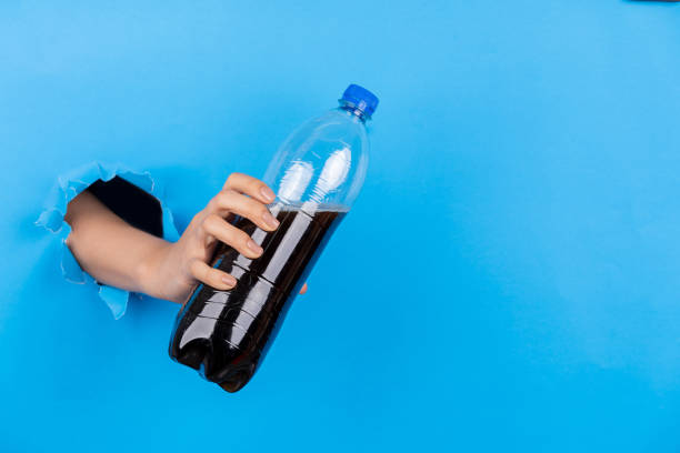 Hand holding plastic bottle through hole in blue paper