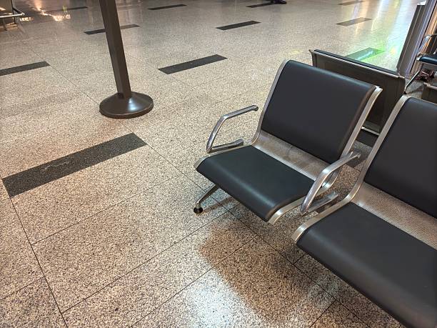 An empty row of black leather airport seats is bathed in warm sunset light, casting long shadows on the wall.