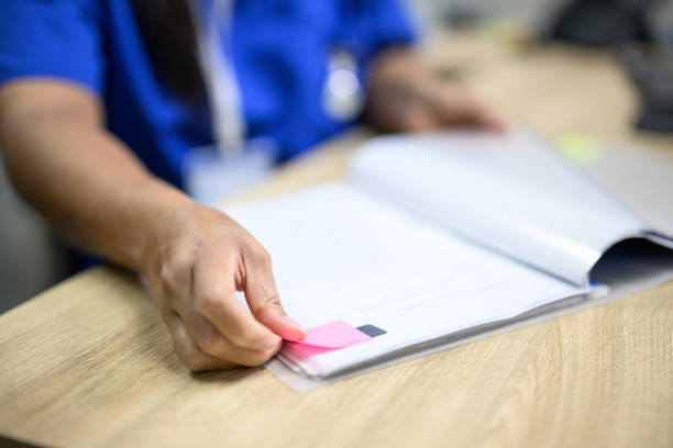 Hospital administrator writing on sticky notes and using laminator in office