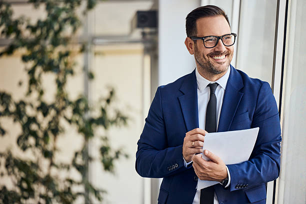 istock Confident Businessman Standing by Window Holding Documents with a Warm Smile 2206511271