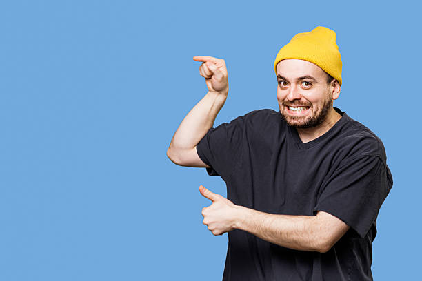 istock Smiling man in yellow beanie pointing against a blue background 2206516007