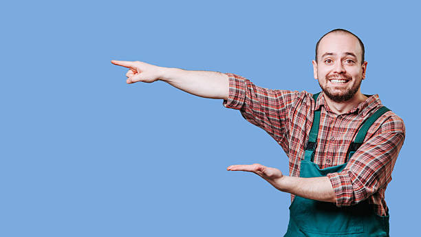 istock Cheerful man in overalls gestures towards the right on a blue background 2206518052