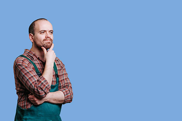 istock Man in green apron pondering actions against blue background 2206518055