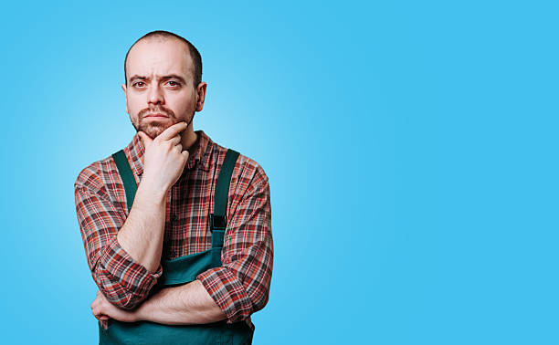 istock Thoughtful man in overalls pondering ideas against blue background 2206518065