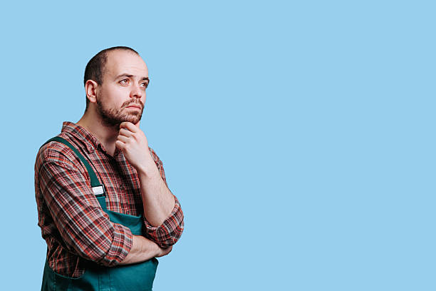 istock Man in green apron deep in thought against a light blue background 2206518080