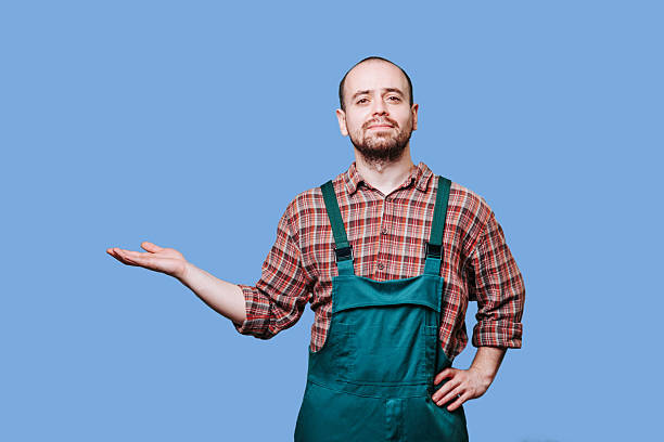 istock Man in green overalls demonstrates relaxed pose against plain blue background 2206518096