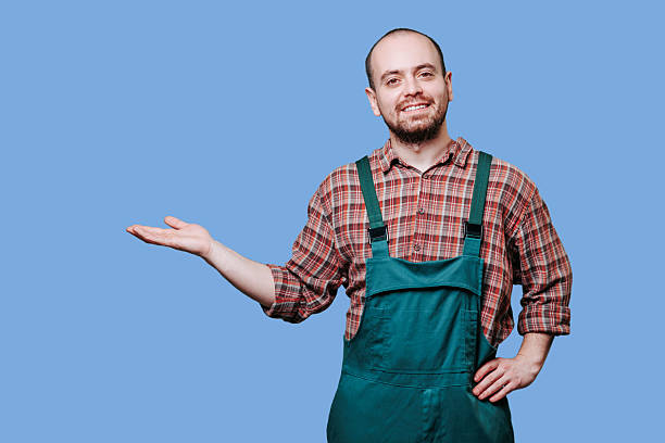 istock Man in green overalls gestures with a friendly smile against a blue backdrop 2206518106