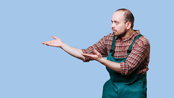 istock Man in green overalls gestures to the side with a serious expression indoors 2206518124