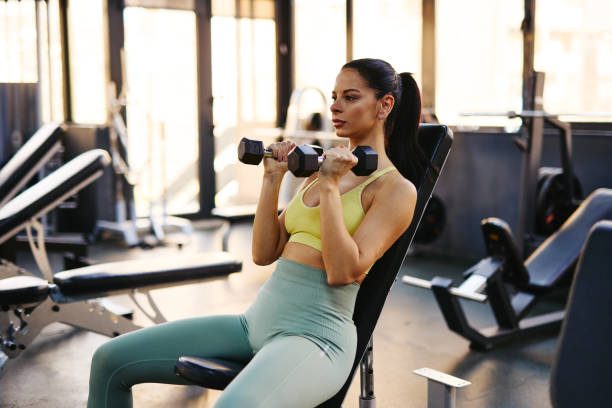 istock Young woman lifting dumbbells while sitting on bench in gym 2206518143