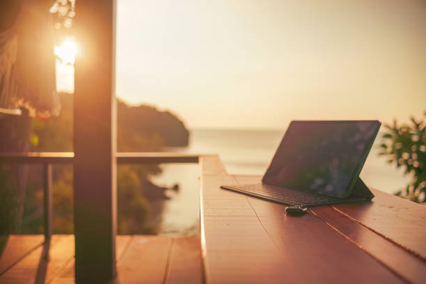 Laptop on wooden table with ocean view at sunrise, remote work concept