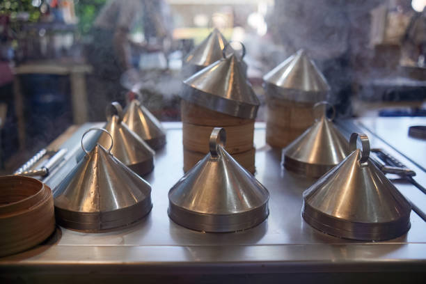 Several dim sum steamers sit ready for use in a restaurant kitchen. Steam rises from the bamboo containers, indicating recent or ongoing cooking activity. Preparation for meal service is evident.