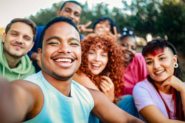istock Young diverse people smiling at mobile phone camera at city park. African nonbinary taking selfie with friends. LGBT community 2206525222