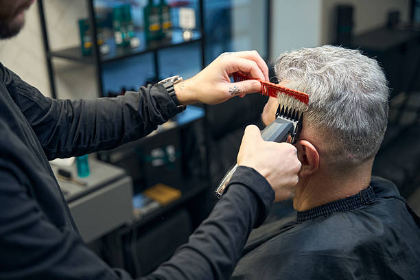 parrucchiere che fa un taglio di capelli a macchina per un cliente maturo con i capelli grigi - tagliare i capelli foto e immagini stock