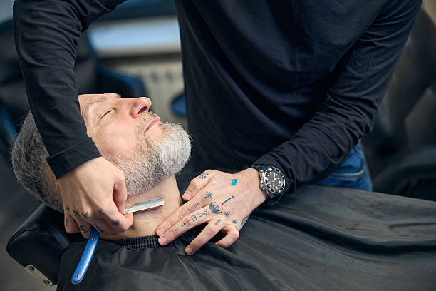 istock Barber using straight razor on neck of gray-haired mature man 2206525704