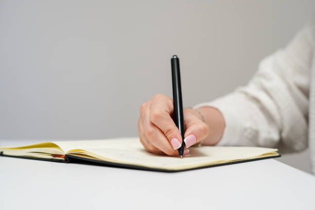 istock a person's hand writing with a black pen in an open notebook on a white desk 2206528400
