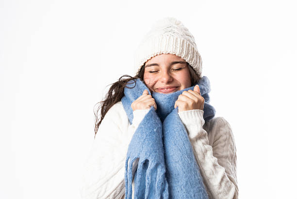 Teenager wearing winter clothes, including a warm hat and scarf, enjoying the cozy feeling against a white background