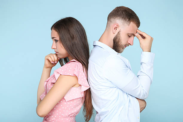 istock Young upset couple standing by the back to each other on blue background 2206538802