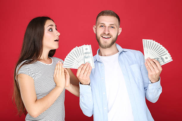 istock Happy young couple with dollar banknotes on red background 2206540517