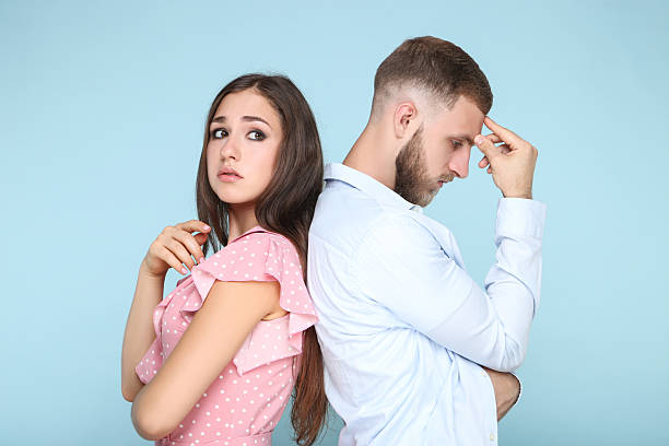 istock Young upset couple standing by the back to each other on blue background 2206540851