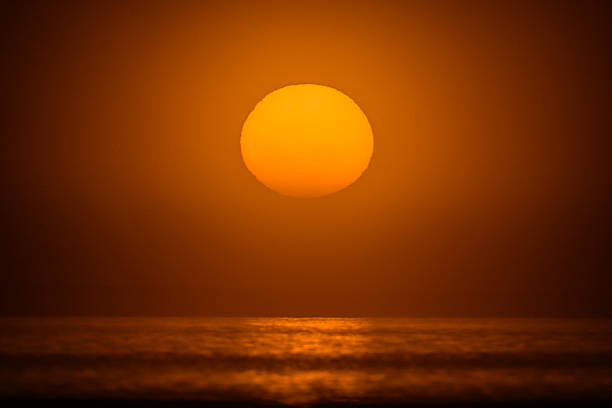 Sunrise through the fog with large orange round sun reflecting on ocean water