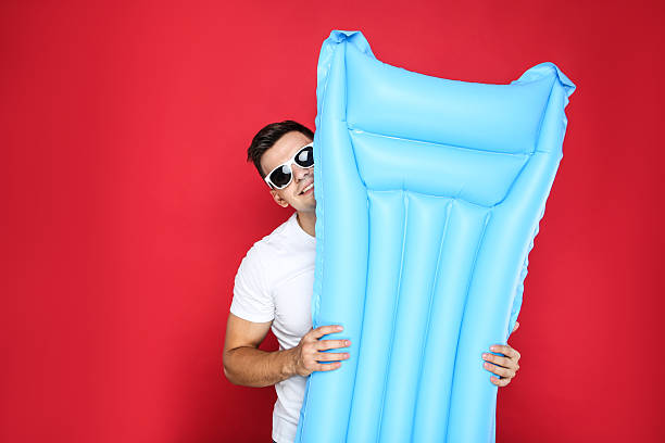 istock Young man in sunglasses holding inflatable mattress on red background 2206548016