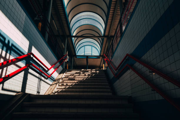 Sunlight illuminates the stairway of an overpass, highlighting the red handrails and tiled walls