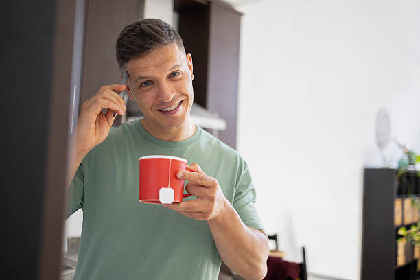 istock Happy man holding red mug and using smartphone in kitchen 2206553481