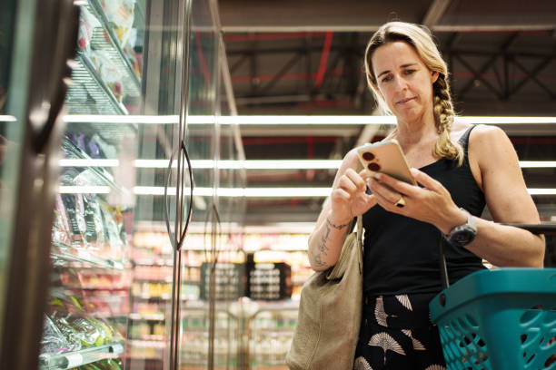 istock Woman using smartphone while holding shopping basket in grocery store 2206558727