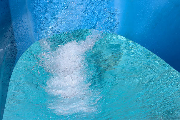 close-up photo capturing the motion of white water moving rapidly down a recreational slide. there is a splash created from the movement. blue and green surfaces with a light effect background