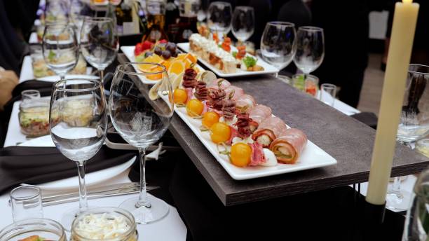 istock Elegant table setting featuring stemmed wine glasses, gourmet canapes, meat rolls, and fruit skewers near glowing candlelight, showcasing upscale event preparation 2206564908
