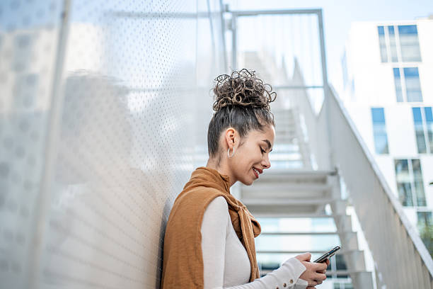 istock Young woman using smartphone leaning against wall in urban setting 2206572009