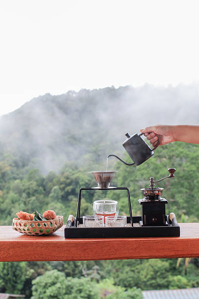 istock Hand pouring hot water on ground coffee with filter, barista using drip coffee set with mountain and fog in morning. 2206580565
