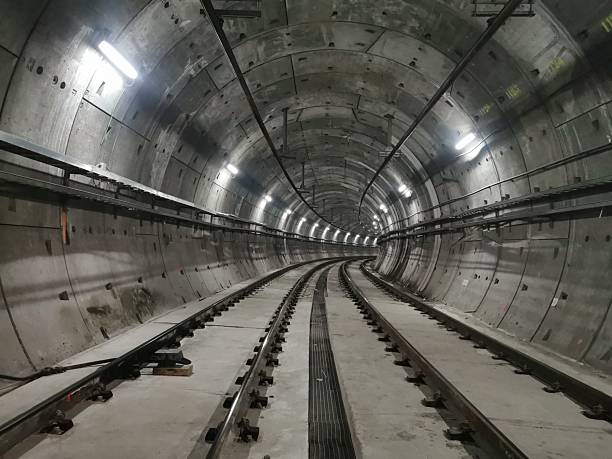 istock Illuminated underground train tunnel with curved tracks turning right. Empty, no trains or people. Industrial infrastructure with cables and lighting. A perspective view of modern subway construction 2206580597