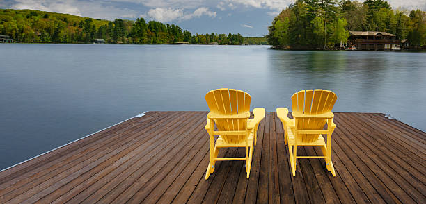 istock Yellow chairs on a dock overlook a calm lake, sky reflected in water. 2206582502