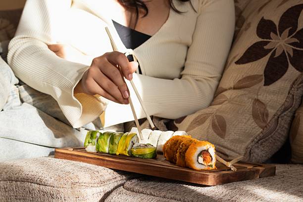 istock unrecognizable latina woman sitting on sofa eating sushi 2206594231