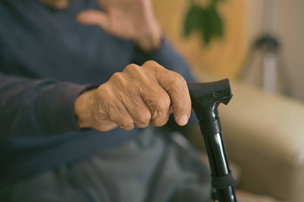 istock Elderly man holding walking stick while sitting on sofa at home: close-up of hand 2206597419
