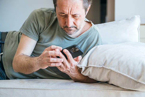 istock Lazy couch potato guy using mobile phone while laying on living room sofa 2206605915